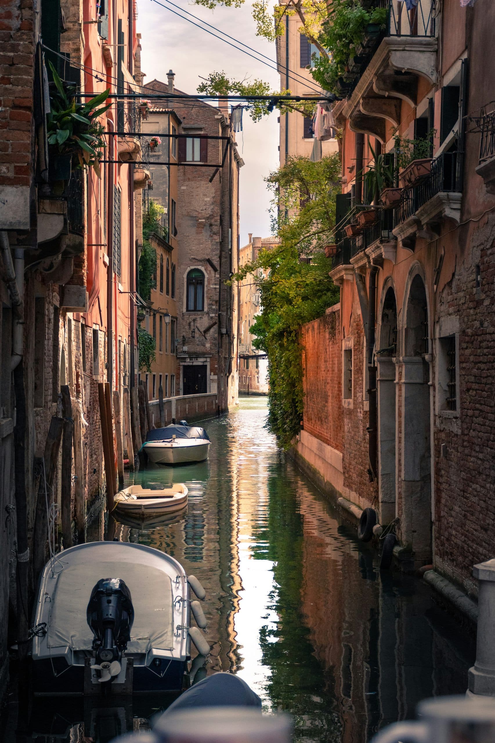 A narrow Venetian canal with small boats moored against brick and plaster buildings, washing hanging above the water.