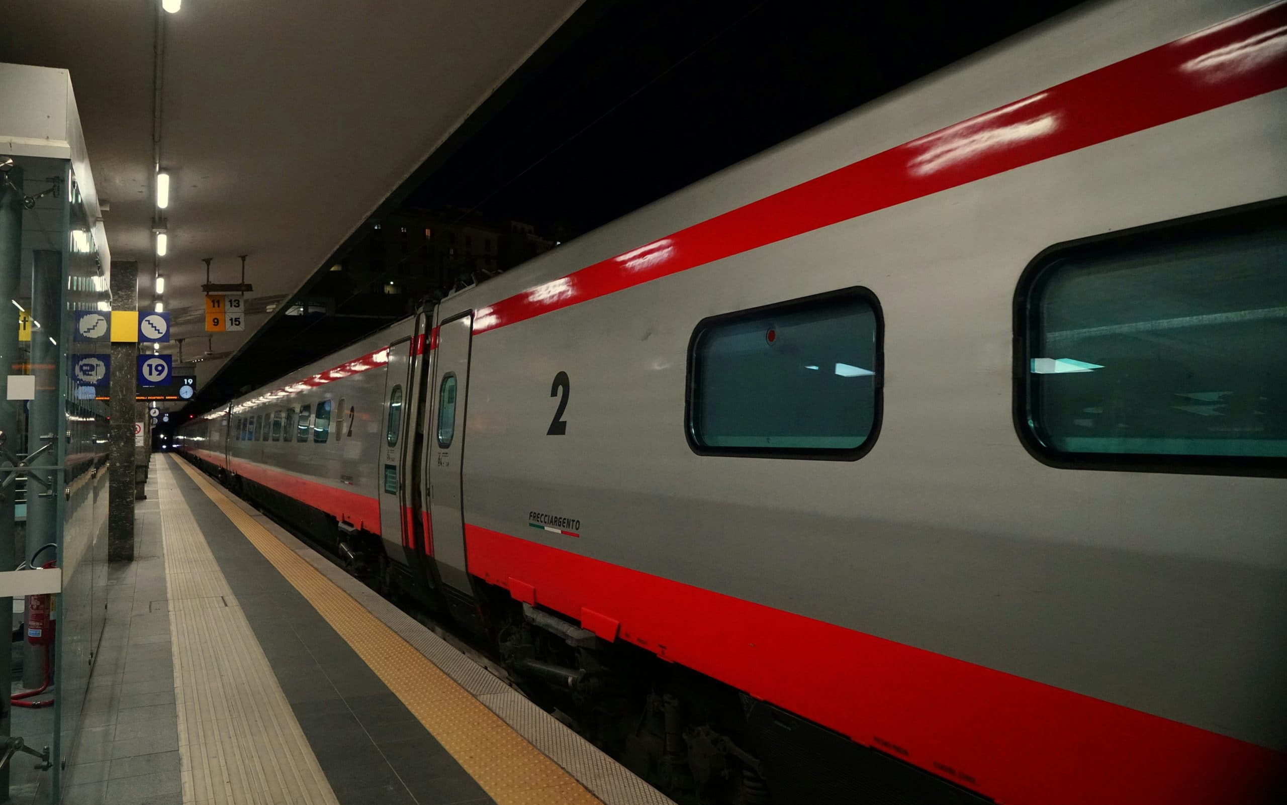 A silver and red Frecciargento high-speed train standing at a covered platform in an Italian station.