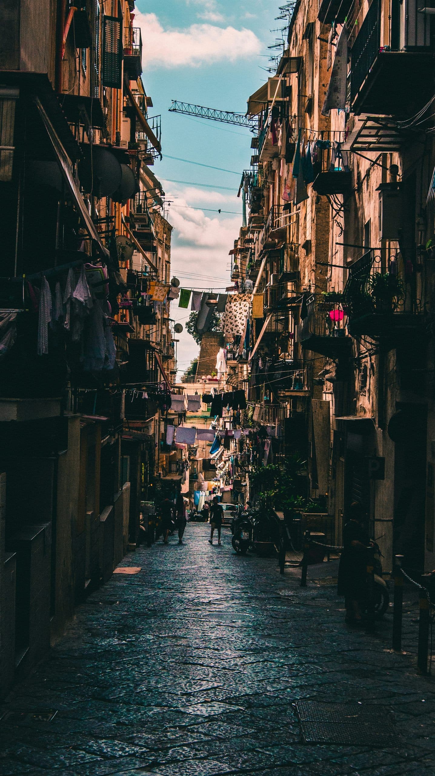 A narrow, shaded alley with washing strung between balconies above a stone-paved street.