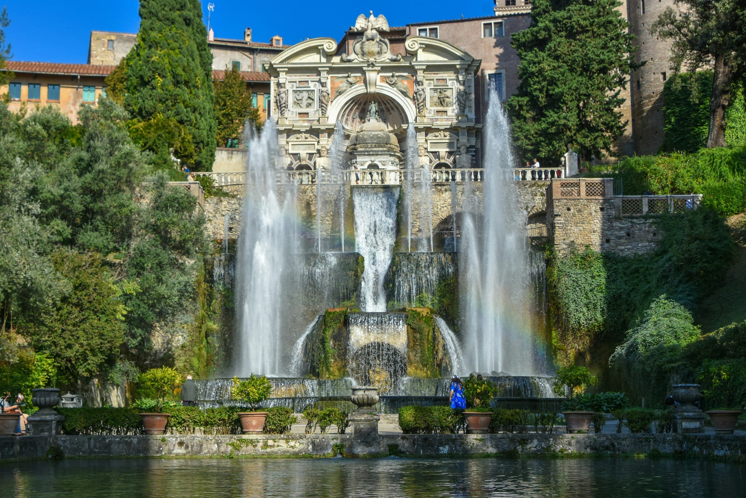 Tall water jets and cascades in front of an ornate stone fountain set into a terraced garden.
